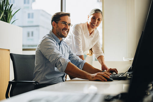 Colleagues smiling and discussing project on computer