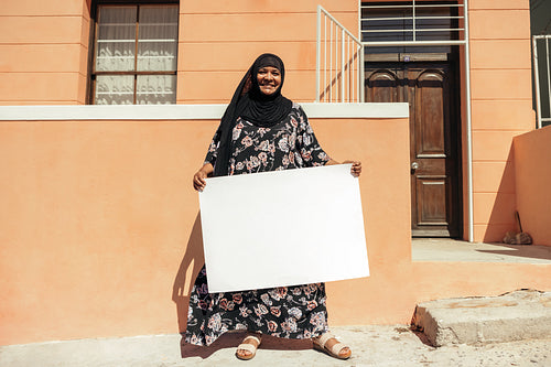 Happy Muslim woman holding a white placard outside her home