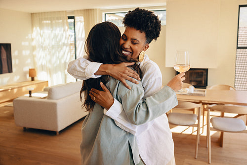 Two women warmly embracing while one holds a glass of white wine