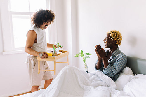 Loving young gay man surprisng his lover with breakfast in bed