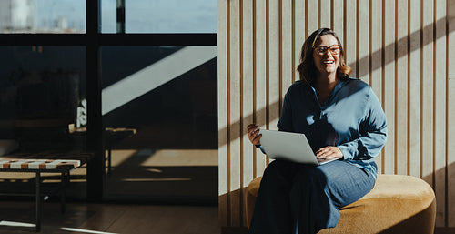 Smiling woman using laptop in sunny modern office environment