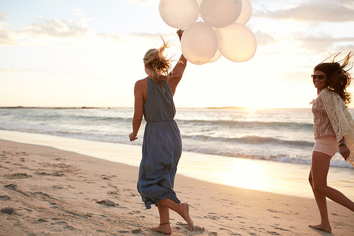 Female friends running on the beach with balloons