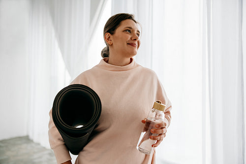 The woman prepares for yoga at home with a mat and water bottle