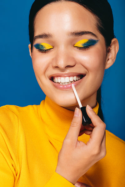 Makeup with a glossy lip: Glamorous young woman applying lip gloss in a studio