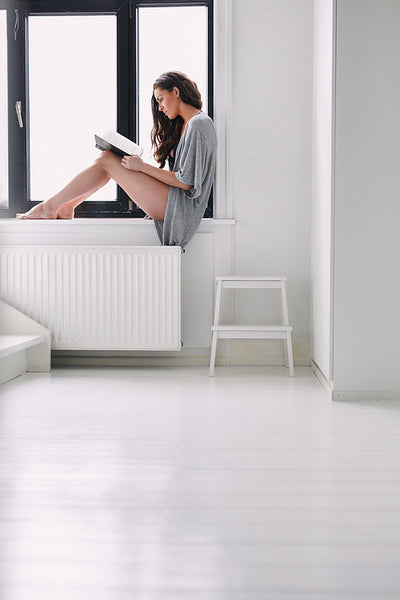 Young woman sitting on window sill reading a book