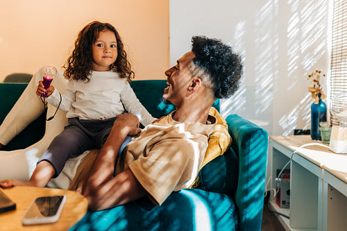 Happy father and daughter having a good time while sitting on a couch at home
