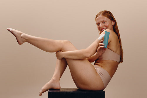Woman applying moisturizer to shoulder while smiling
