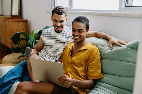 Happy couple using a laptop together on a sofa at home