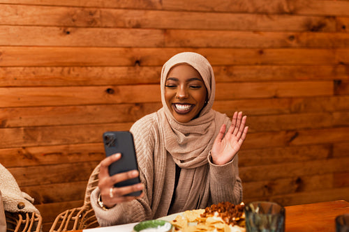 Cheerful muslim woman having a video call in a restaurant