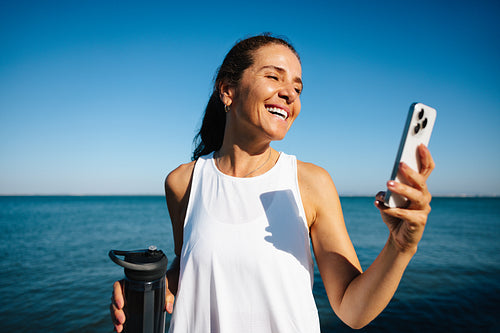 Happy woman enjoying a moment by the sea with her smartphone