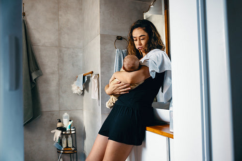 Mother brushes teeth while holding baby in bathroom