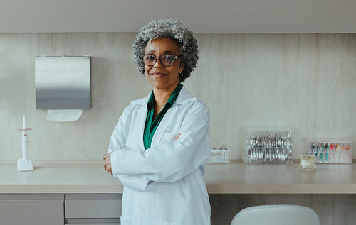Female dentist stands in a clinical setting wearing a white coat