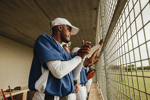 Baseball players standing in the dugout, watching the game intently with anticipation