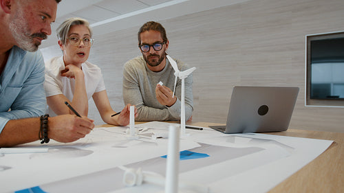Engineers working on a wind energy project in an office, discussing blueprints and 3D windmill models