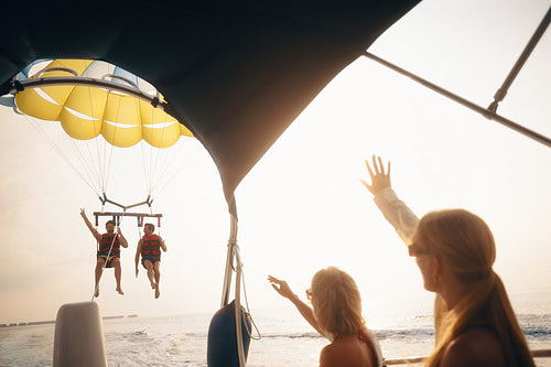 People waving from a boat to friends parasailing over the ocean during a sunny vacation