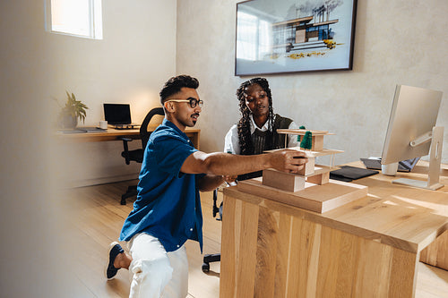 Two architects discussing a wooden architectural model in a modern office space