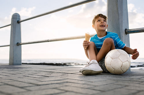 Boy eating an ice cream sitting near seafront
