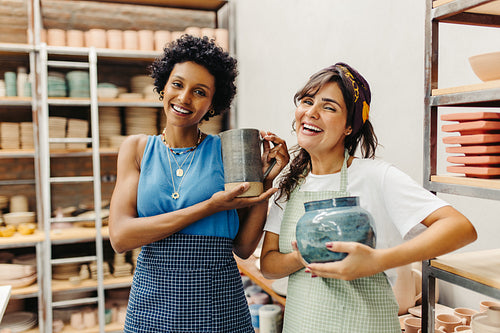 Happy female potters holding their handmade ceramic products