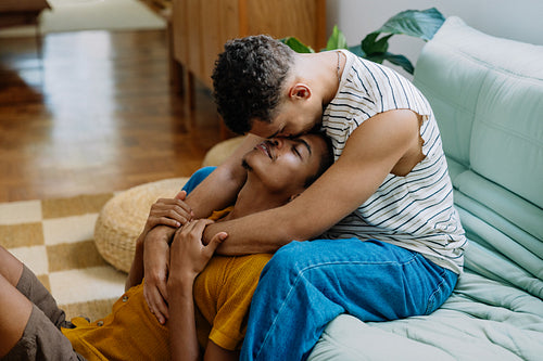 Romantic moment of a gay couple embracing peacefully on their cozy couch