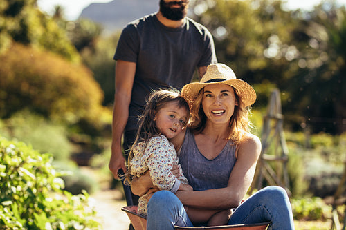 Mother and daughter ride in wheelbarrow pushed by father
