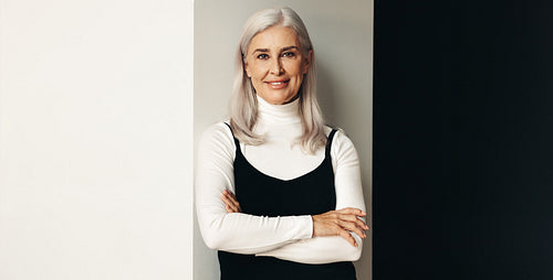 Portrait of a confident senior woman with silver hair, standing against studio background