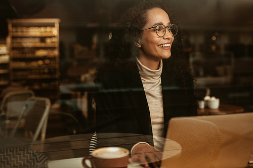 Businesswoman looking outside cafe window and smiling