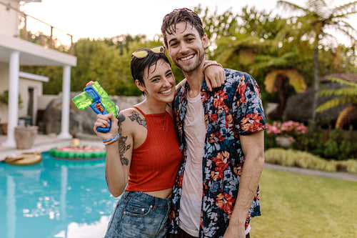 Fully wet couple by the pool with a water gun