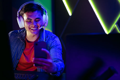 Happy young gamer watching live game broadcasts on a gaming app using his smartphone