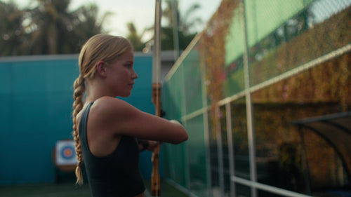 Blonde female archer in athletic wear aiming a bow and arrow with determination