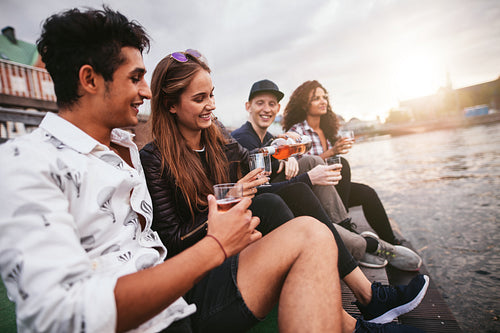 Friends sitting outdoors on jetty and having drinks