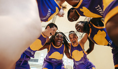 Excited young basketball players huddling on indoor court for motivation and bonding