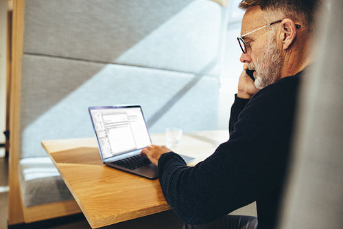 Mature businessman looking at a laptop screen during a phone cal