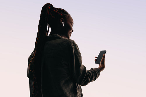 Rearview of a young woman smiling while using a smartphone app for a video chat in a studio