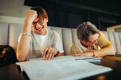Joyful study session between student and lecturer laughing over educational materials in a cozy environment