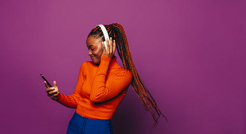 Happy gen z woman dancing with headphones and phone on purple background.