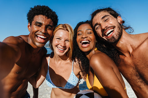 Group of young friends enjoying a summer day taking a selfie at the beach in swimsuits