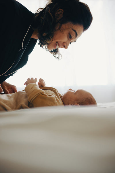 Mother smiles at baby lying on bed