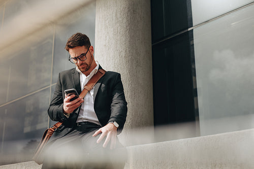 Entrepreneur sitting outdoors typing message on his cell phone