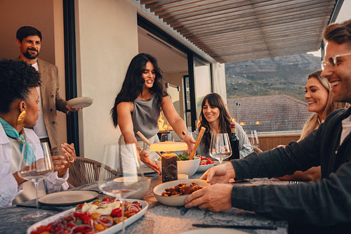 Friends enjoying a casual summer dinner together on a terrace during the evening