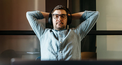 Relaxed young man using headphones while seated in a modern workspace