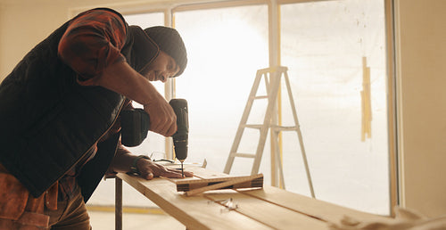 Man working with a drill gun to secure a wood plank for trim work