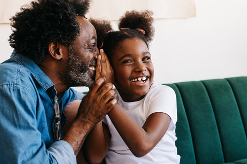 Father whispering to his daughter at home, having a fun moment