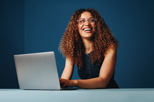 Blue studio tones frame a woman working on a laptop with a smiling expression