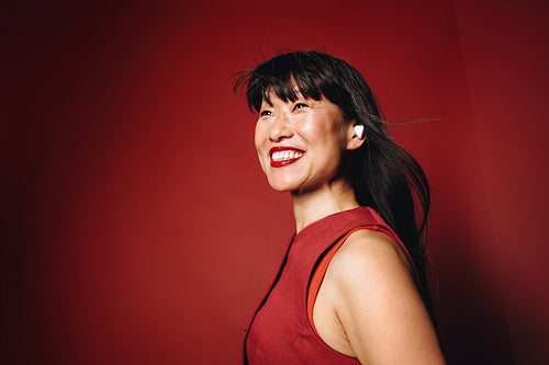 Music surrounds the woman in a red studio portrait with an earbud