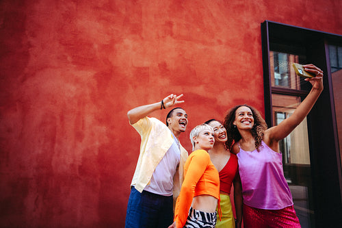 Friends take a smartphone selfie together outdoors against a bright wall