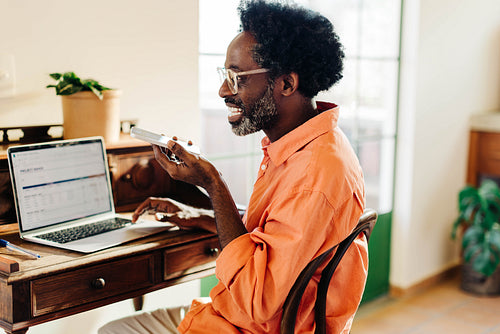 Mature man working remotely from home on laptop and having a phone call