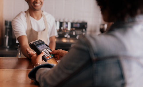 Customer entering pin number into machine at counter in cafe