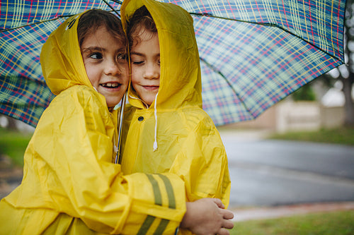 Adorable girls in raincoats hugging each other under umbrella