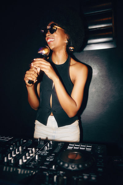 Woman singing passionately with microphone in stylish outfit under dim lighting