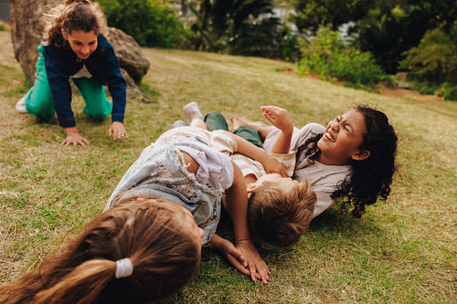 Group of joyful children laughing and playing together on grass in a park